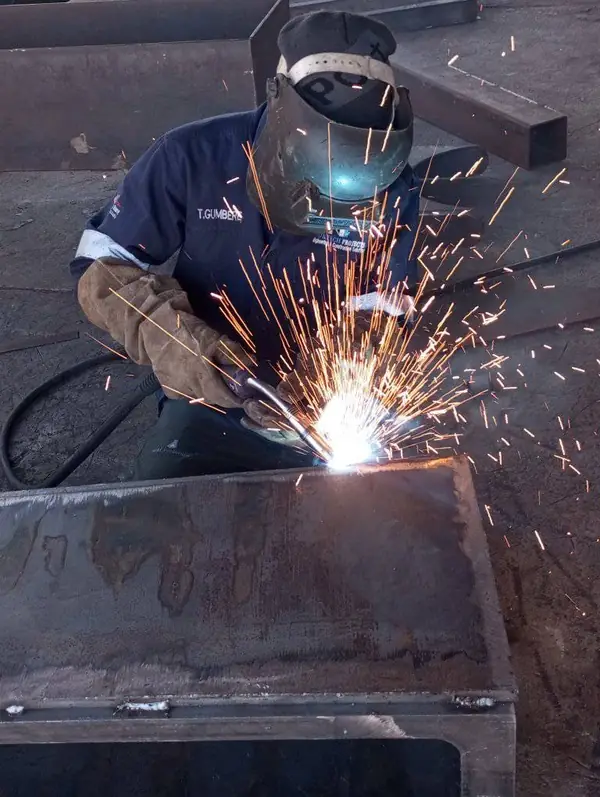 Welder in a welding helmet MIG welding a heavy steel section